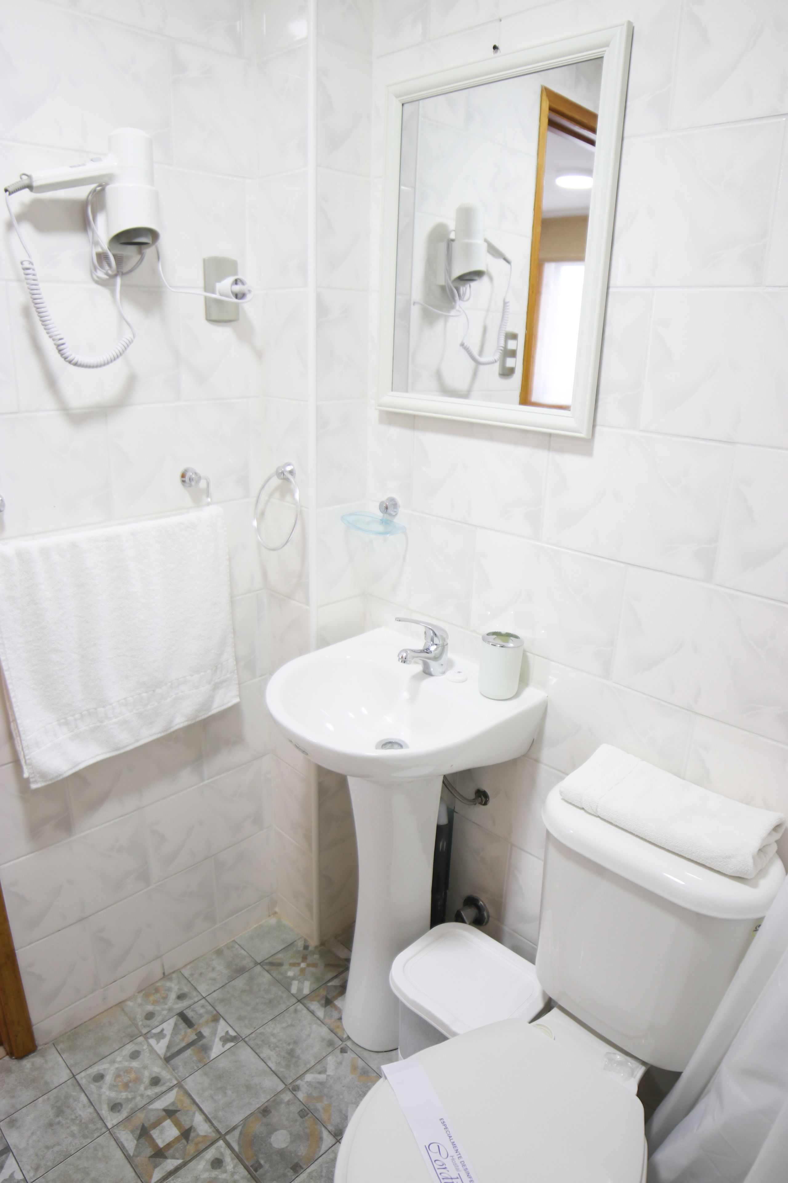 A bathroom with a toilet, sink, and hairdryer mounted on the wall.