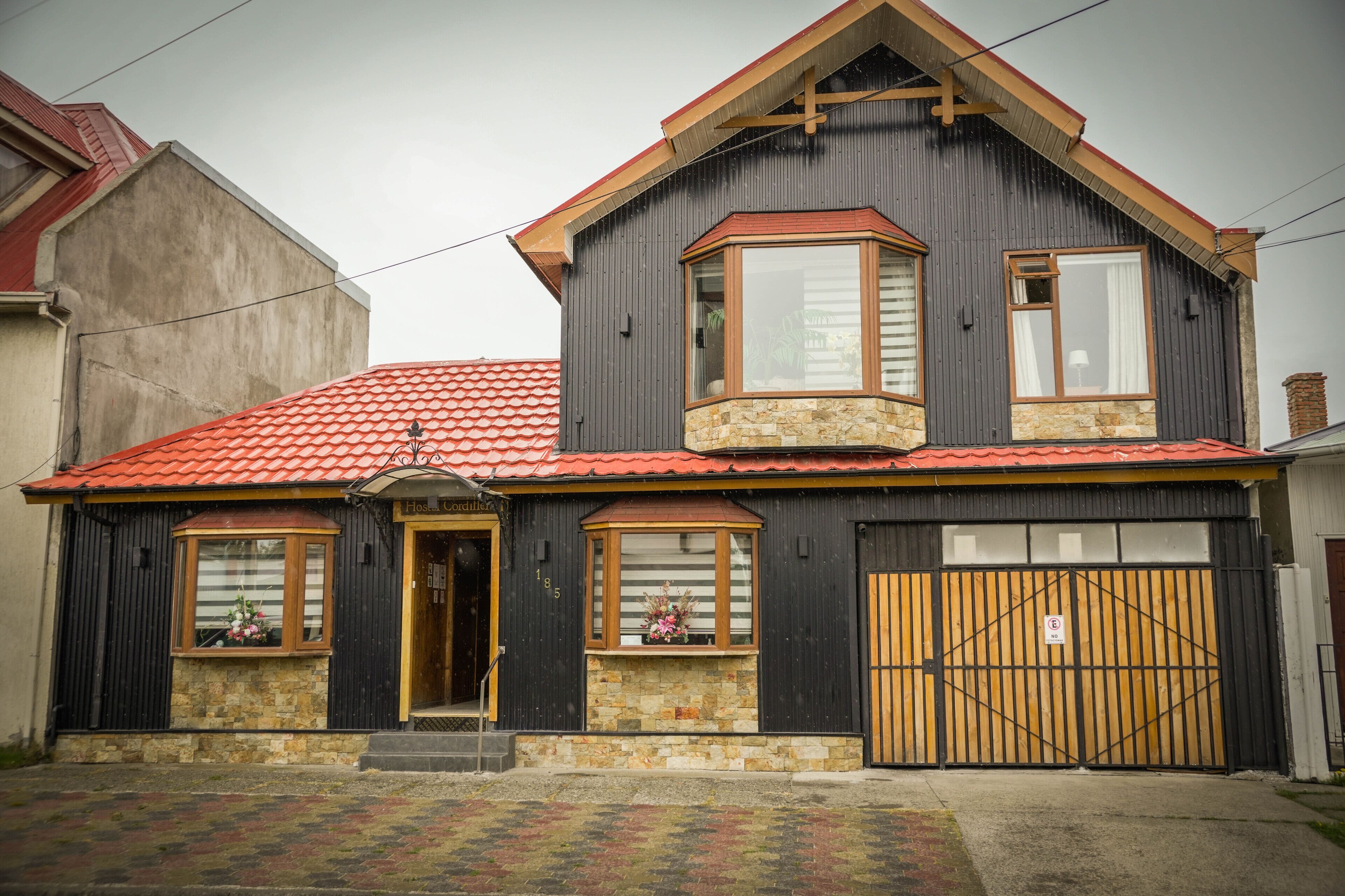 A two-story house with a red-tiled roof, a stone foundation, and a large wooden gate.