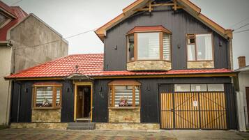 A two-story house with a red-tiled roof, a stone foundation, and a large wooden gate.