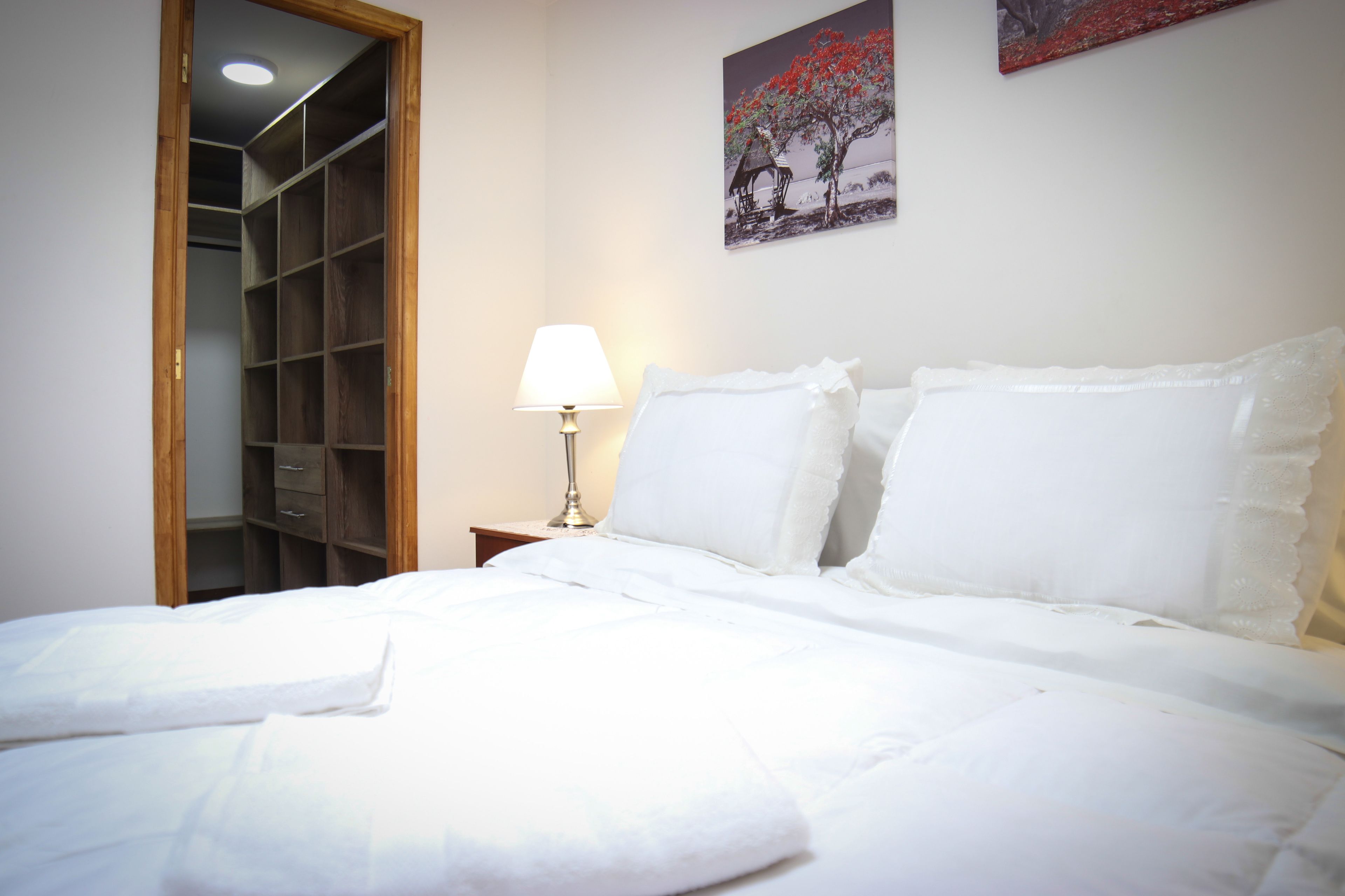 A neatly made bed with white linens, a bedside lamp, and a wooden wardrobe.