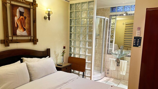 Hotelkamer met een bed, een schilderij, een vaas met een roos, een douche en een badkamer met een glazen wastafel.