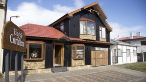 Een gebouw met twee verdiepingen, een rode pannendak, een groot erkerraam en een houten voordeur.