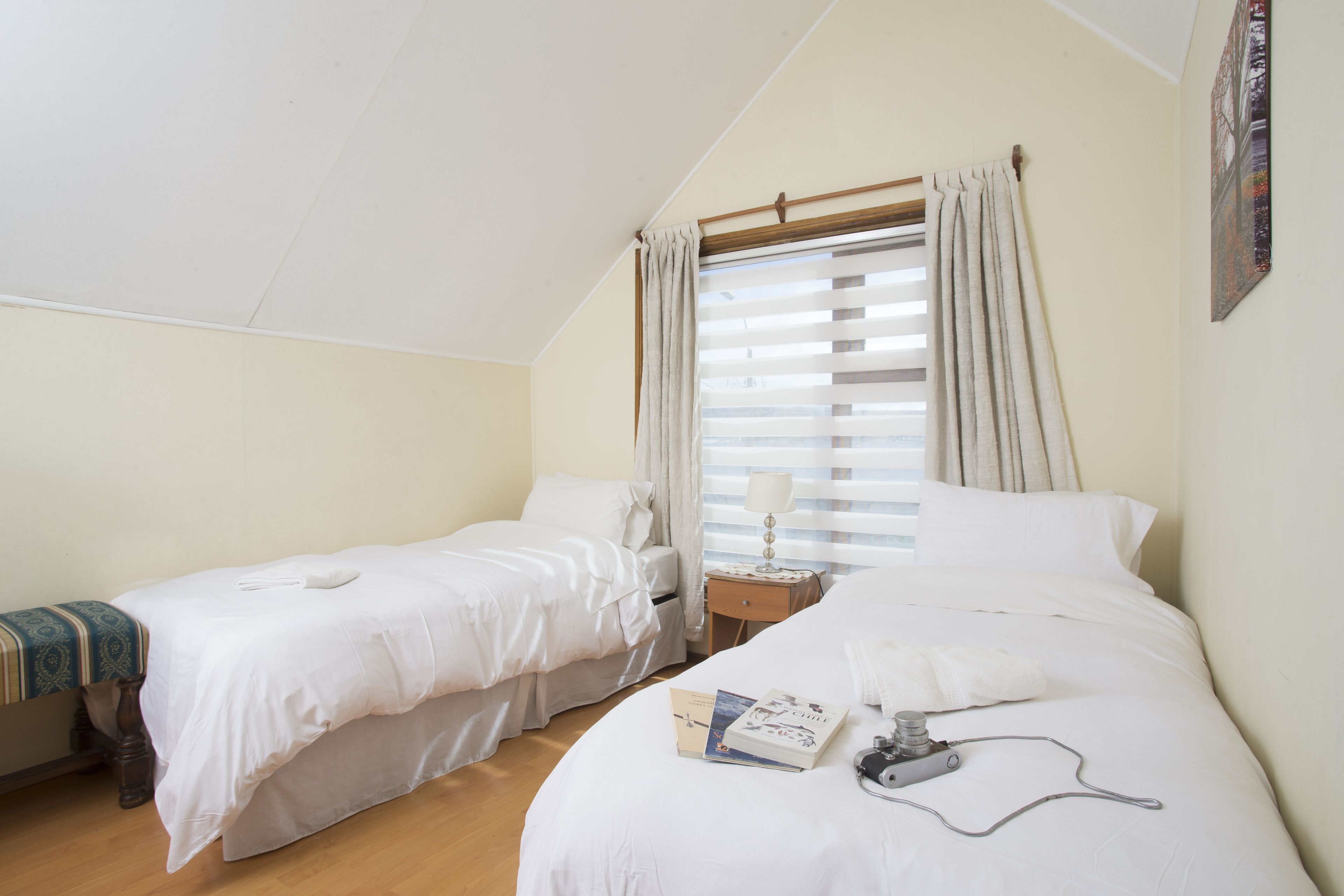 Un dormitorio con dos camas individuales, una mesita de noche con lámpara y una ventana con persianas.