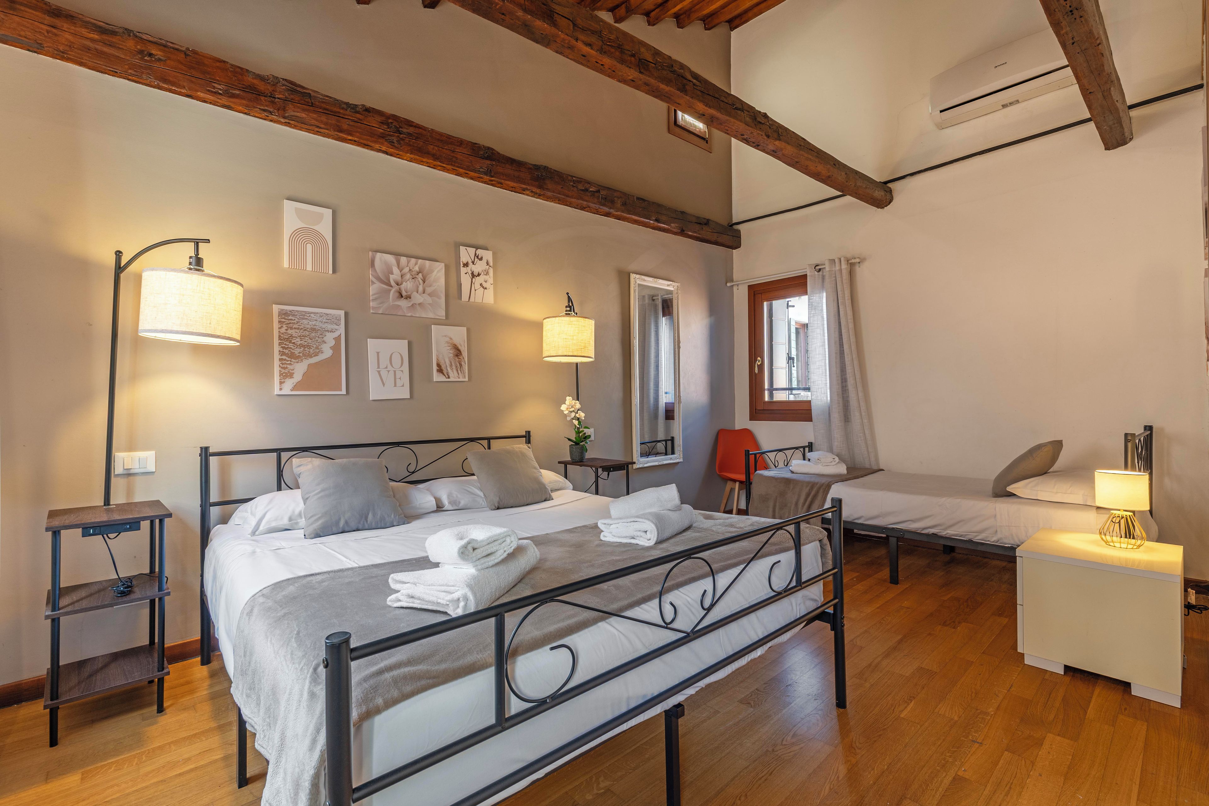 Un dormitorio con una cama grande, una cama más pequeña, un escritorio y una silla. Hay lámparas de pared y obras de arte.