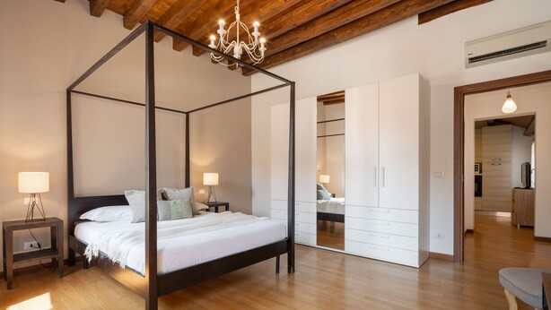 A four-poster bed with a wooden frame, bedside tables with lamps, and a wardrobe with mirrored doors. - Design Palace Apartment by Wonderful Italy (Venice)