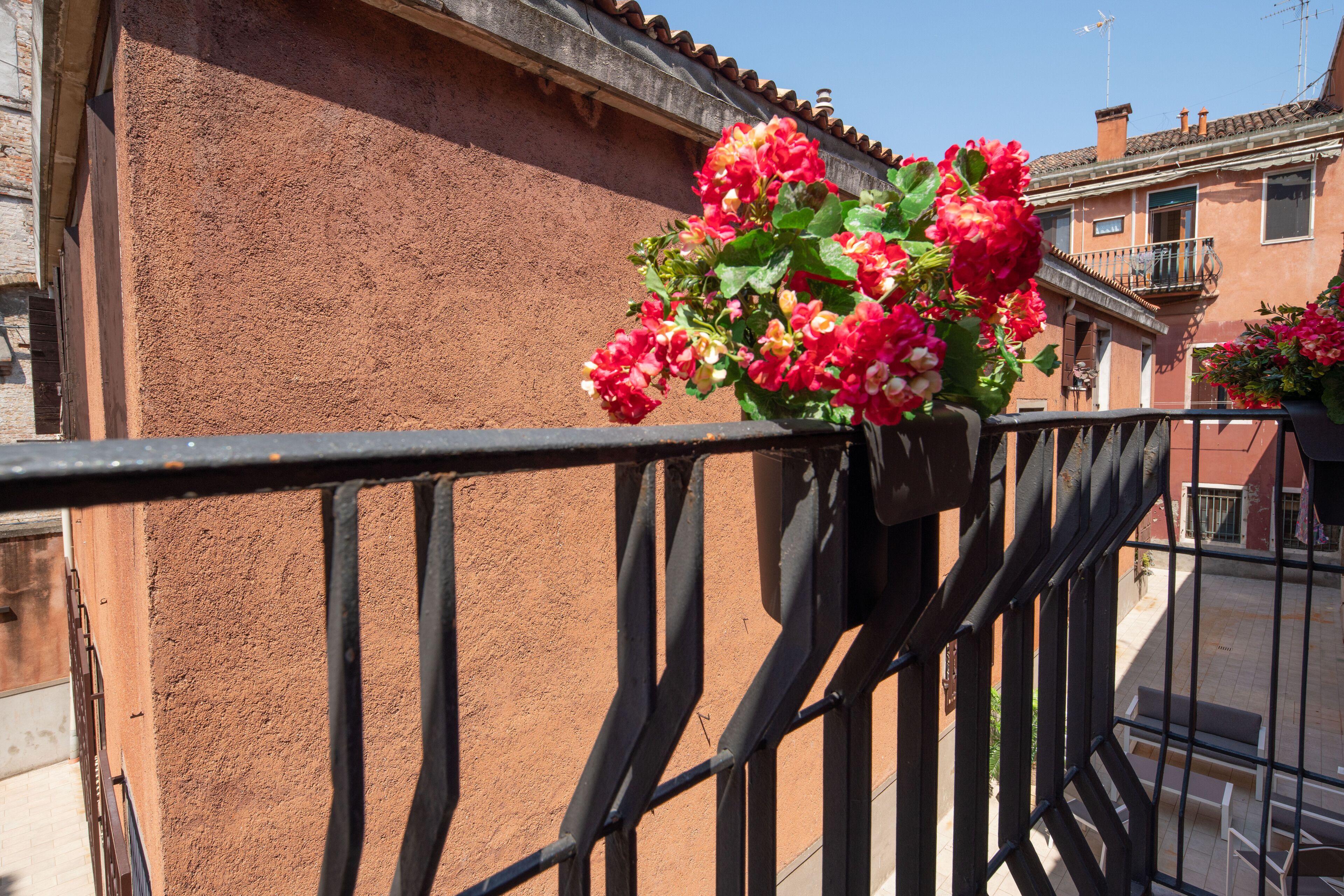 Ein Balkon mit Metallgeländer und einem Blumentopf mit roten Blüten.