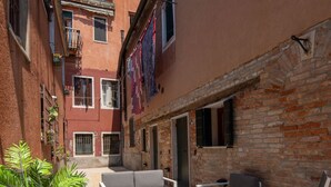 A courtyard with outdoor seating, a brick wall, and a tiled floor. - Design Palace Apartment by Wonderful Italy (Venice)