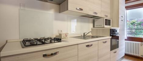 A modern kitchen with a gas stove, microwave, oven, and a window with a view of flowers.