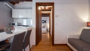 A modern kitchen with white cabinets, a dining table with chairs, and a microwave. A wooden door leads to a bedroom with a bed and a nightstand. - Design Palace Apartment by Wonderful Italy (Venice)