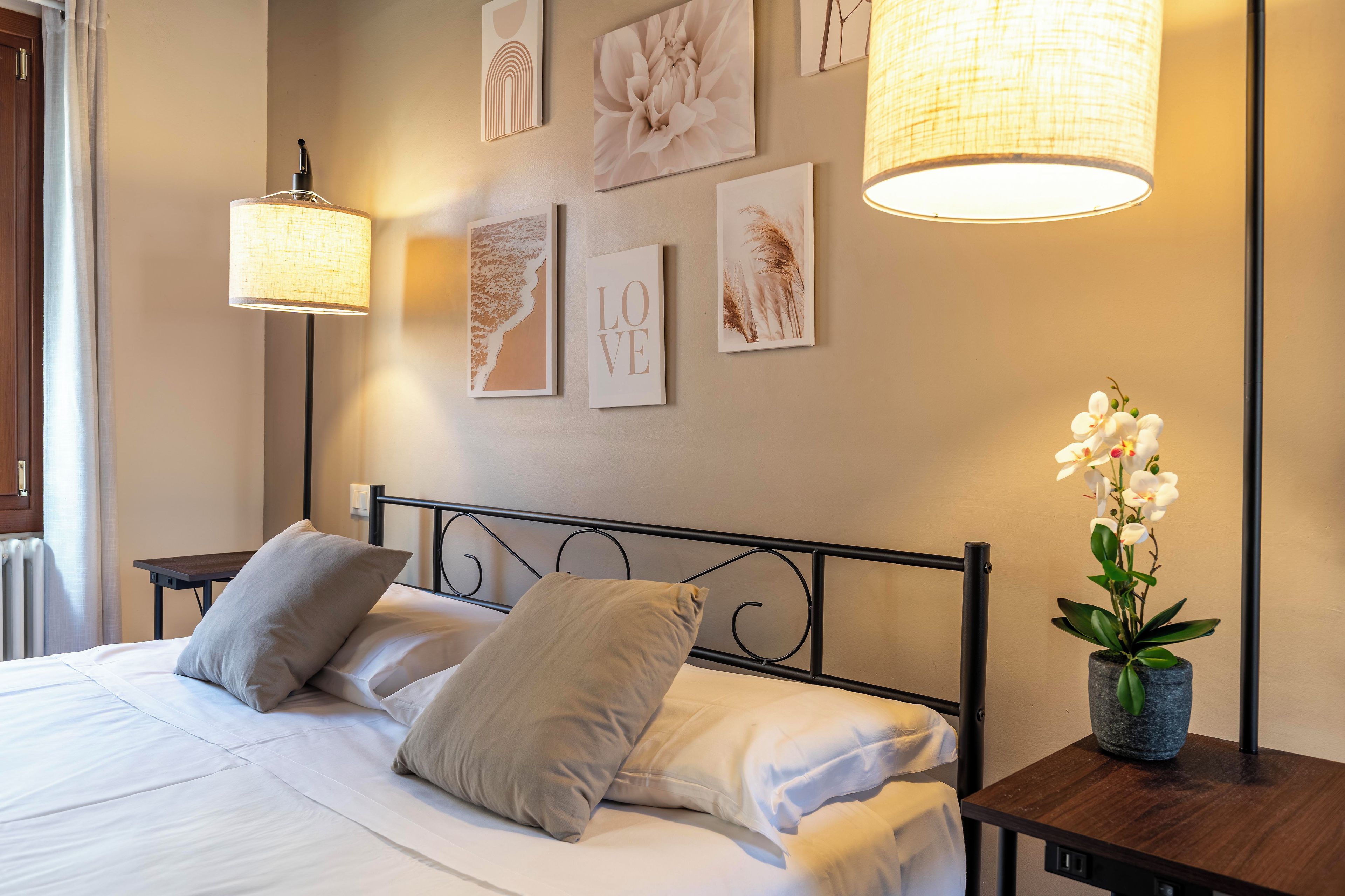 A neatly made bed with pillows, a bedside table with a lamp, and wall art including a 'LOVE' sign.