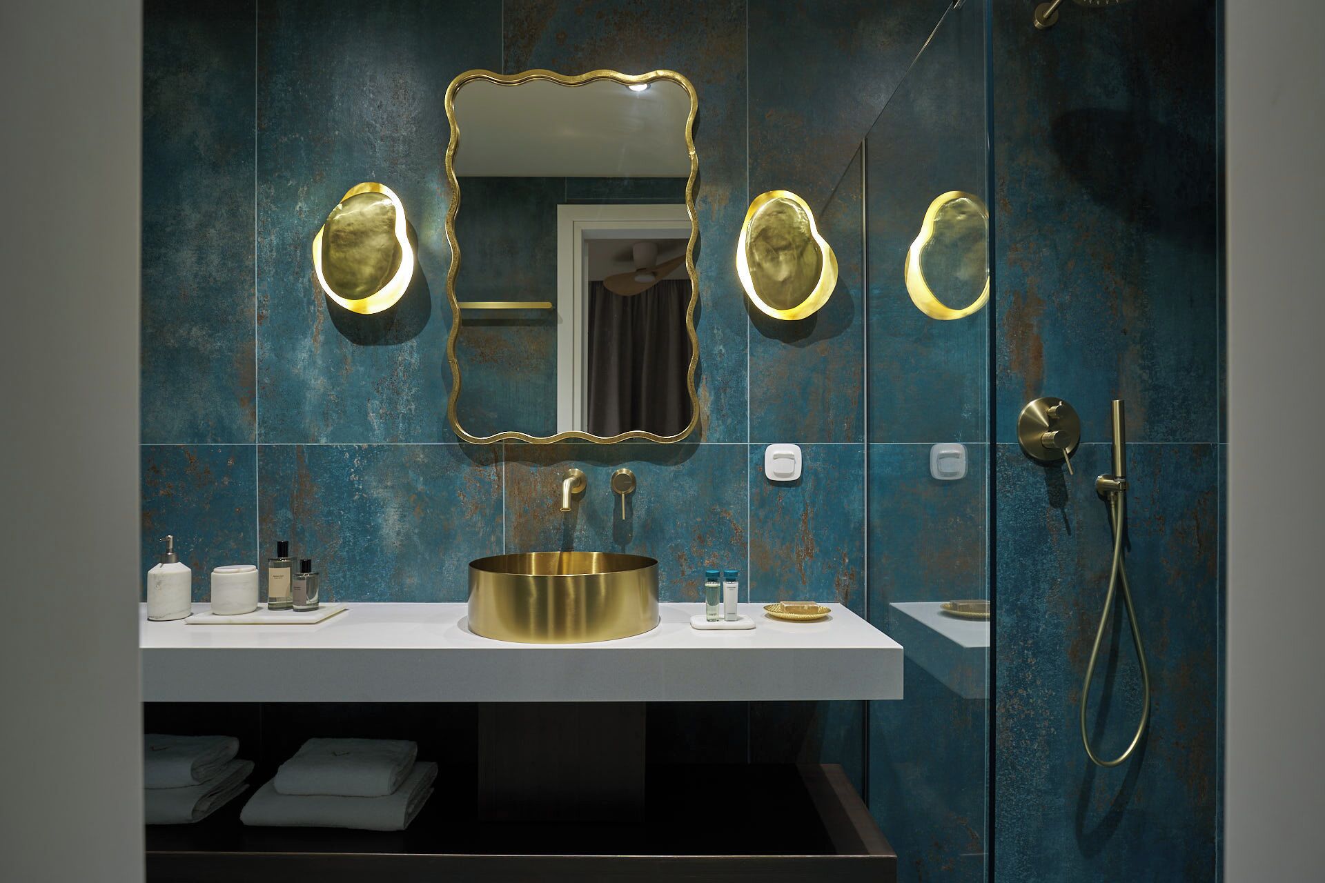 A bathroom with a gold sink, a large mirror with gold trim, and a shower with a gold showerhead.