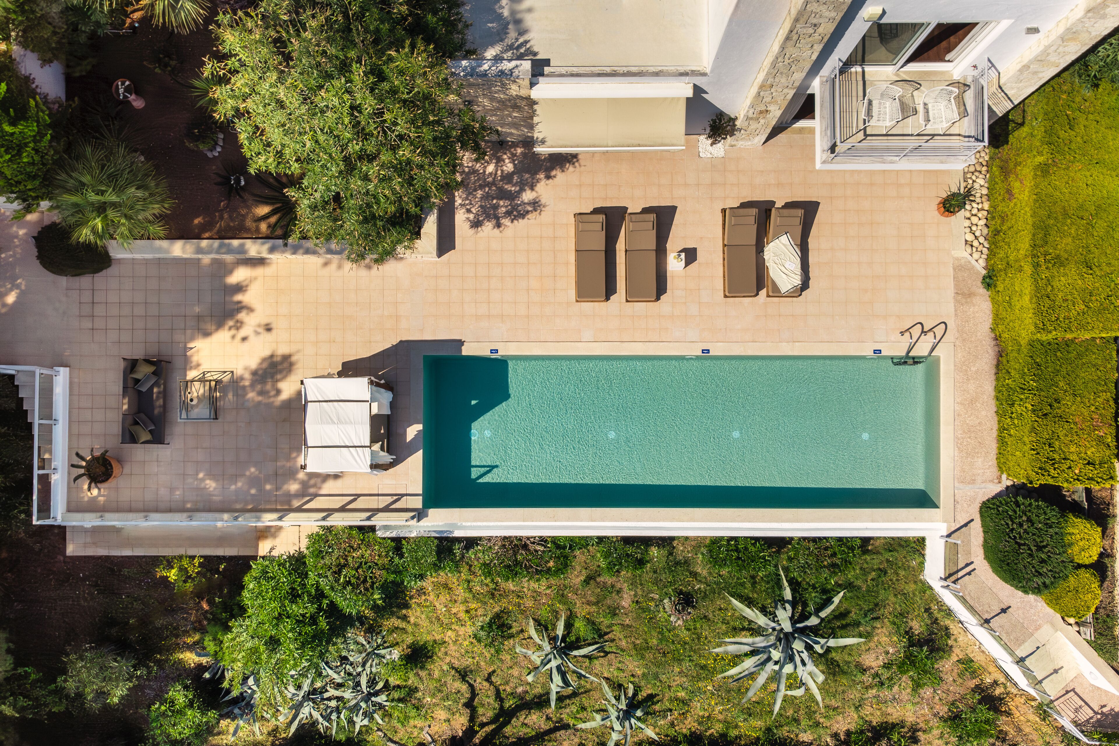 An aerial view of a modern hotel with a swimming pool, sun loungers, and a well-maintained garden.