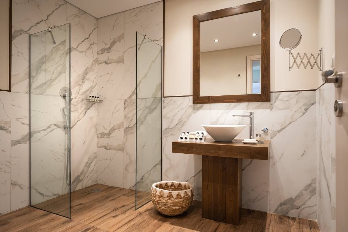 Un baño moderno con ducha de vidrio, tocador de madera con lavamanos blanco y un espejo grande sobre el lavamanos.