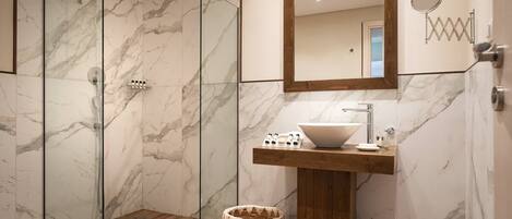 Un baño moderno con ducha de vidrio, tocador de madera con lavamanos blanco y un espejo grande sobre el lavamanos.