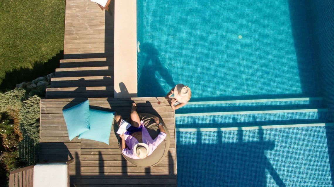 Vue aérienne d’une piscine avec une terrasse en bois, une chaise longue et un parasol.
