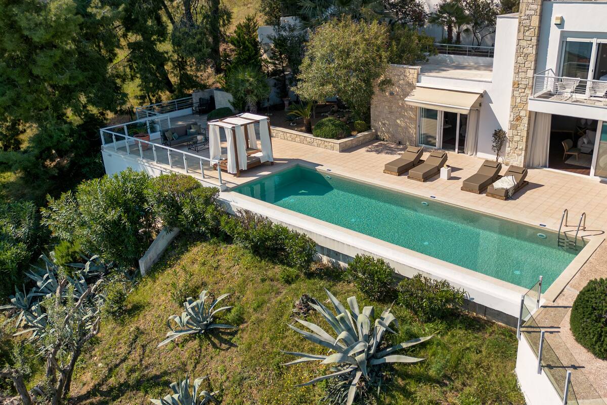 A modern poolside area with a clear pool, lounge chairs, and a covered seating area.