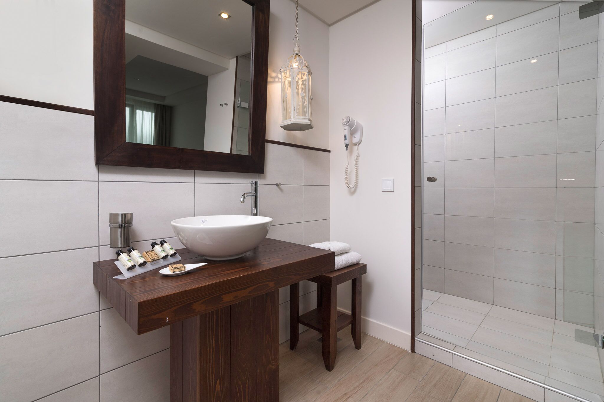 A modern bathroom with a large mirror, a wooden vanity, a white sink, and a glass shower enclosure.