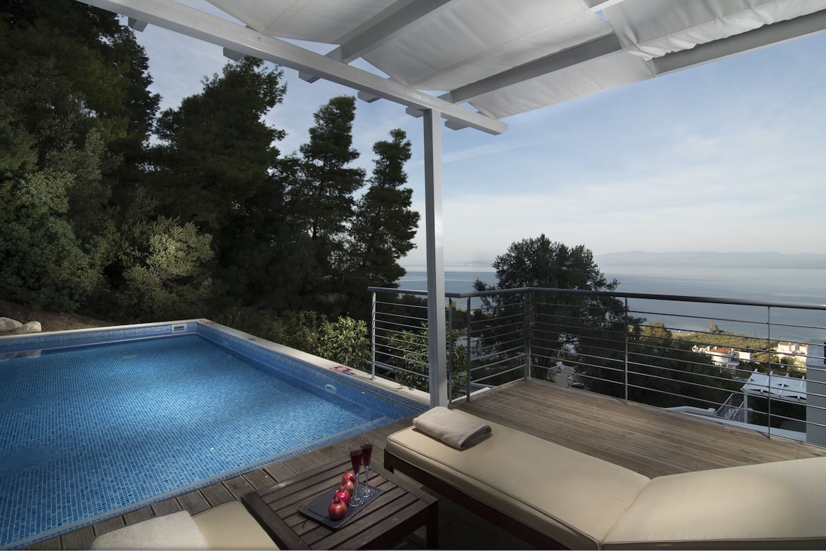 A rooftop pool with a view of the sea, a lounge area with a table and drinks, and a covered patio.