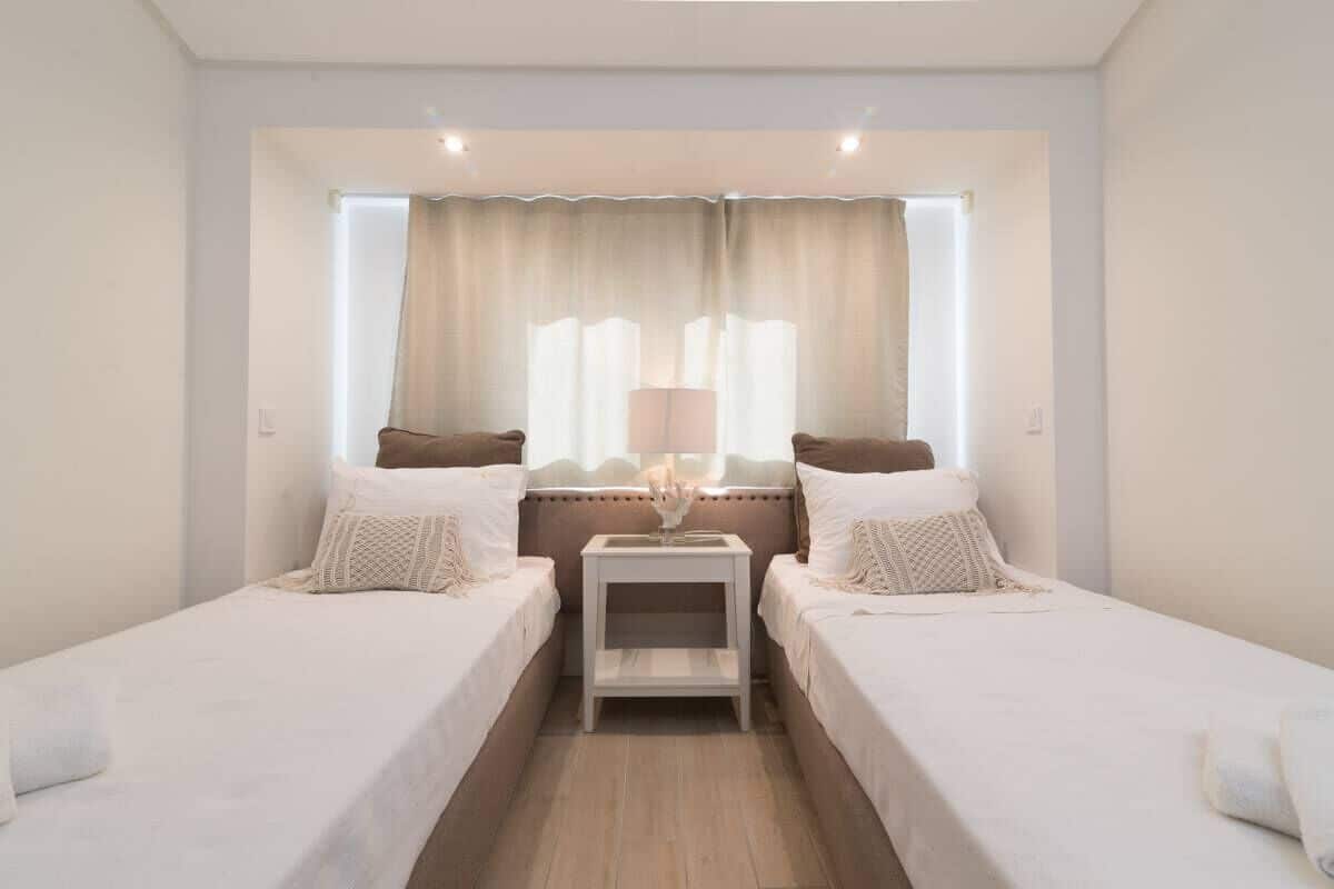 A twin room with two beds, a bedside table, a lamp, and a window with curtains.
