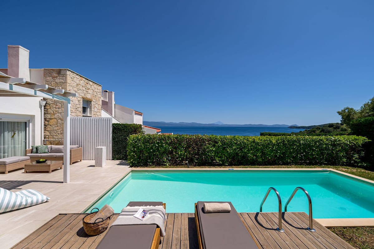 A modern pool area with lounge chairs, a wooden deck, and a stone wall.