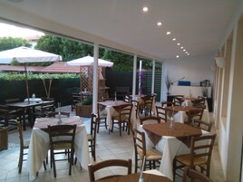 Un área de comedor al aire libre con varias mesas y sillas, cubierta por sombrillas y rodeada de vegetación.