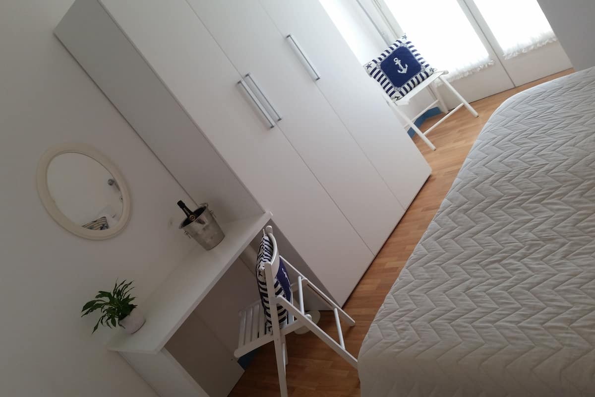 A bedroom with a bed, a wardrobe, a mirror, a plant, and a small table with a chair.