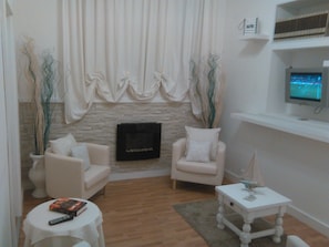 A living room with two armchairs, a small table, a fireplace, and a television on a shelf. - Hotel Milano (Pietrasanta)