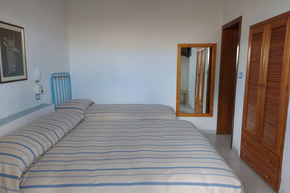 A bedroom with a bed, a bedside table, a mirror, and a wardrobe.