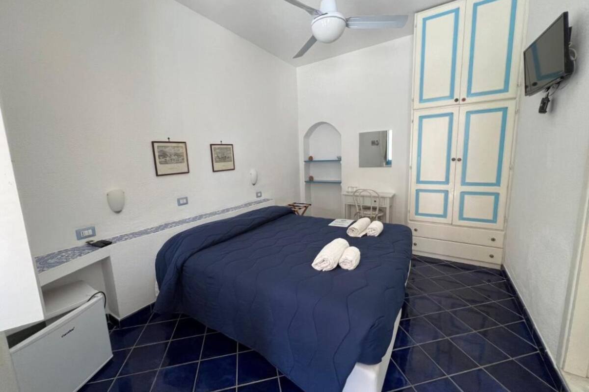 A hotel room with a bed, a desk, a chair, a wardrobe, a television, and a ceiling fan.