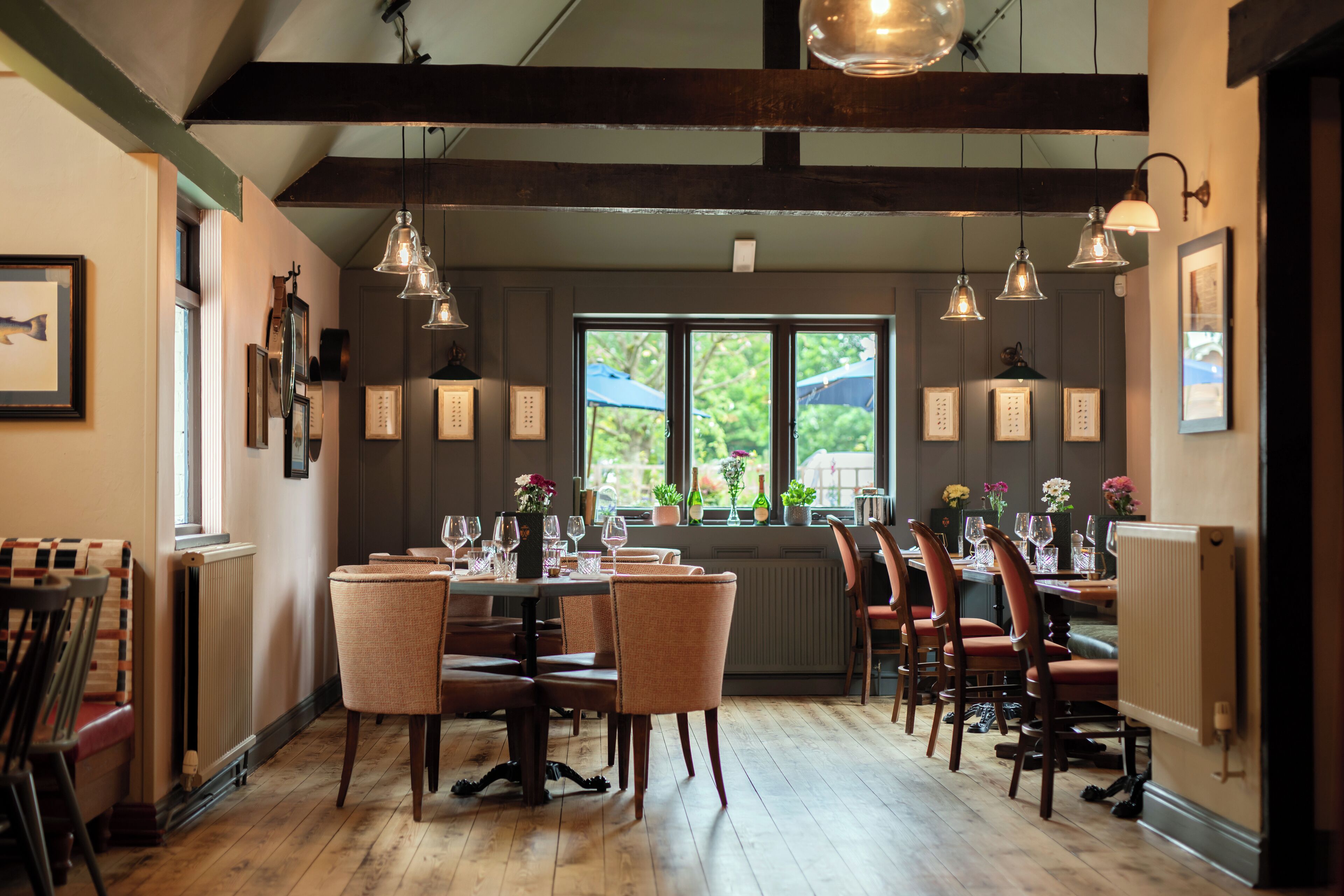 Un espace repas avec des tables et des chaises en bois, des luminaires suspendus et des tableaux encadrés aux murs.