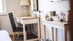 Una habitación pequeña y ordenada con escritorio, silla, lámpara y espacio para preparar café.