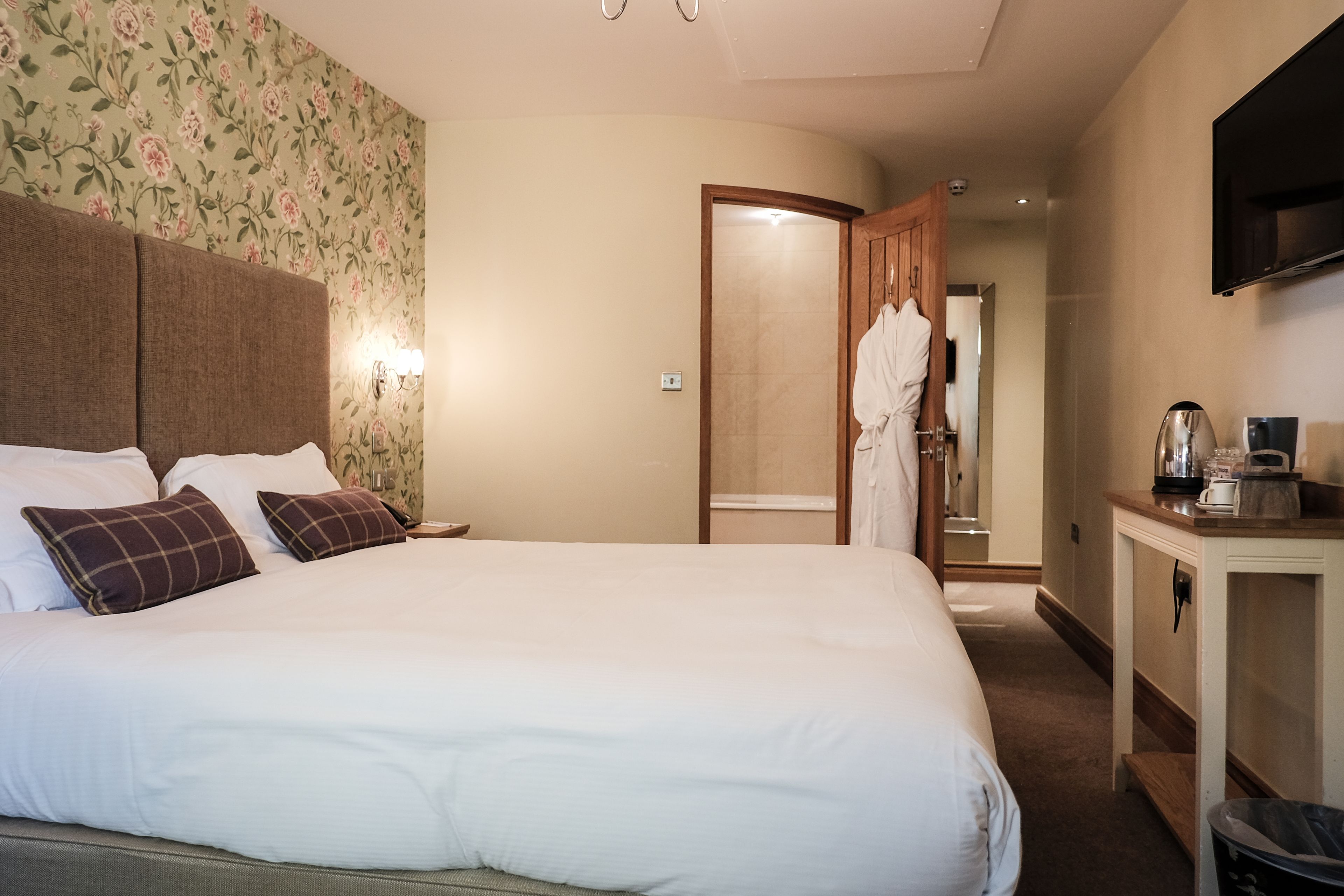 Ein Hotelzimmer mit einem großen Bett, einem Holzkopfende, einem an der Wand montierten Fernseher und einem kleinen Tisch mit einer Kaffeemaschine.