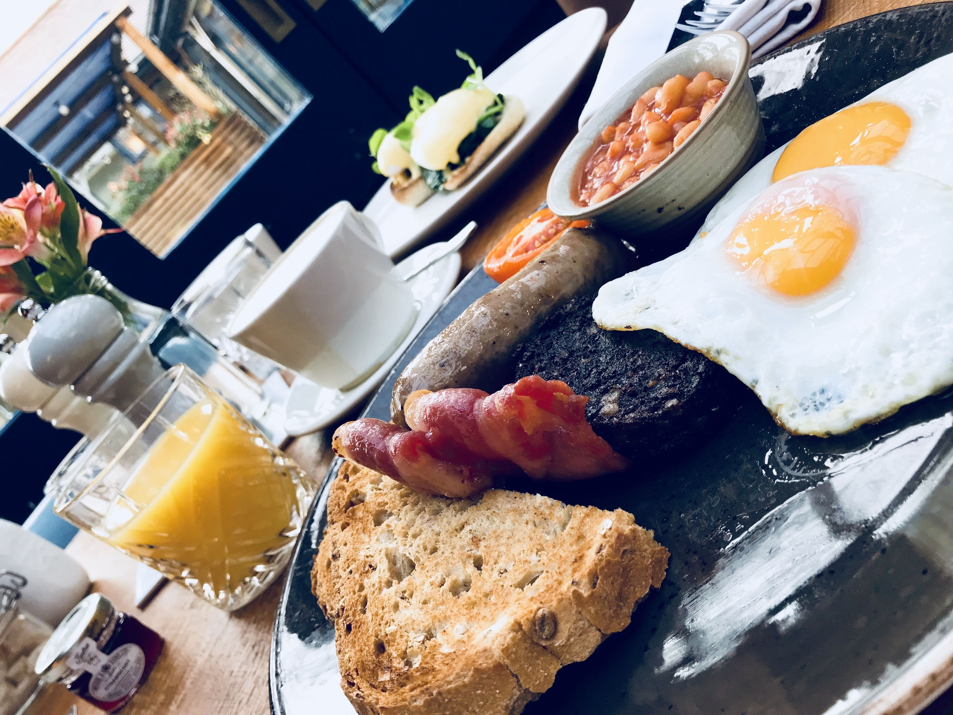 A breakfast plate with eggs, bacon, beans, toast, and a glass of orange juice.