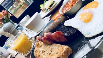A breakfast plate with eggs, bacon, beans, toast, and a glass of orange juice.