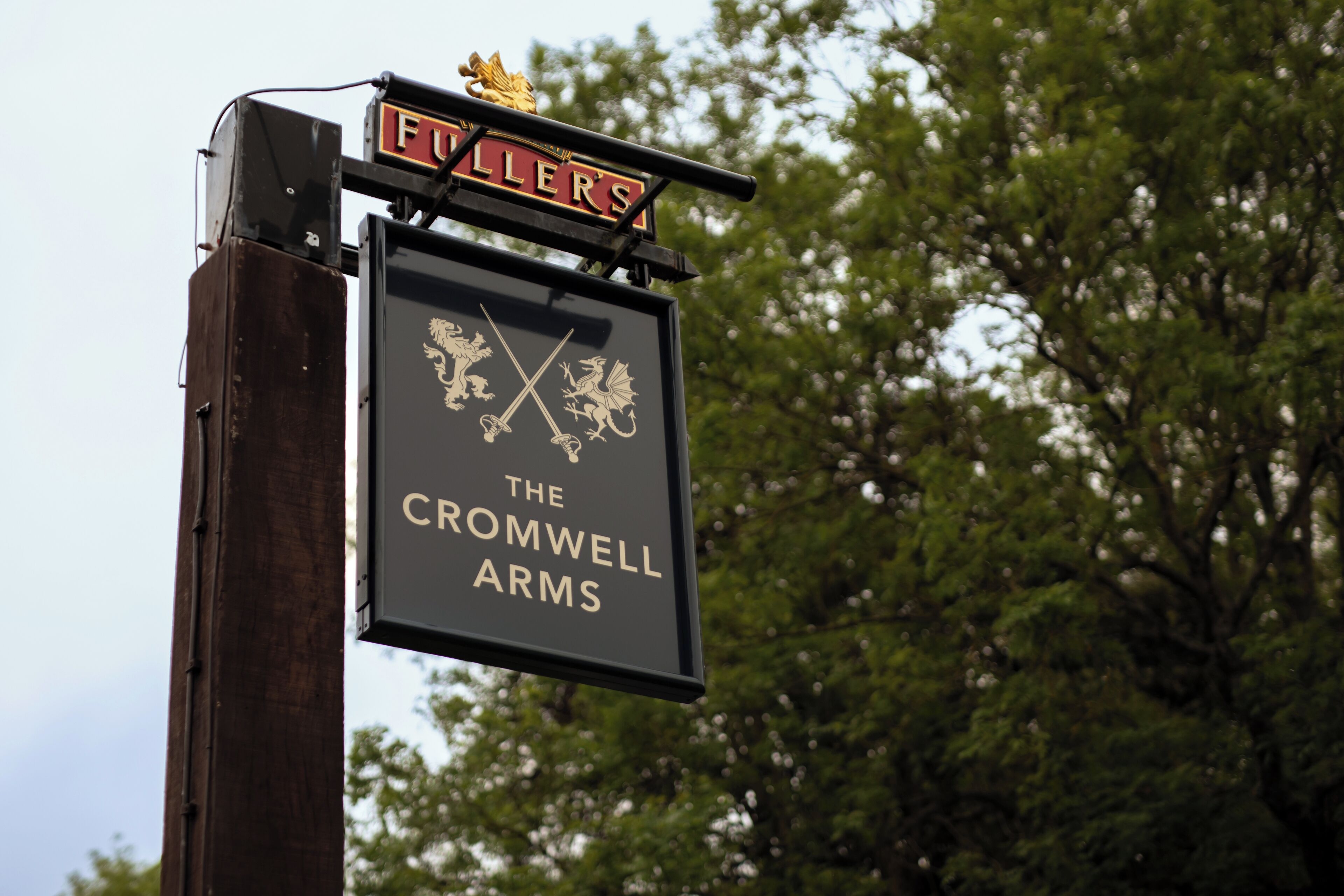 A sign for 'The Cromwell Arms' pub with a coat of arms and a gold emblem above the name.