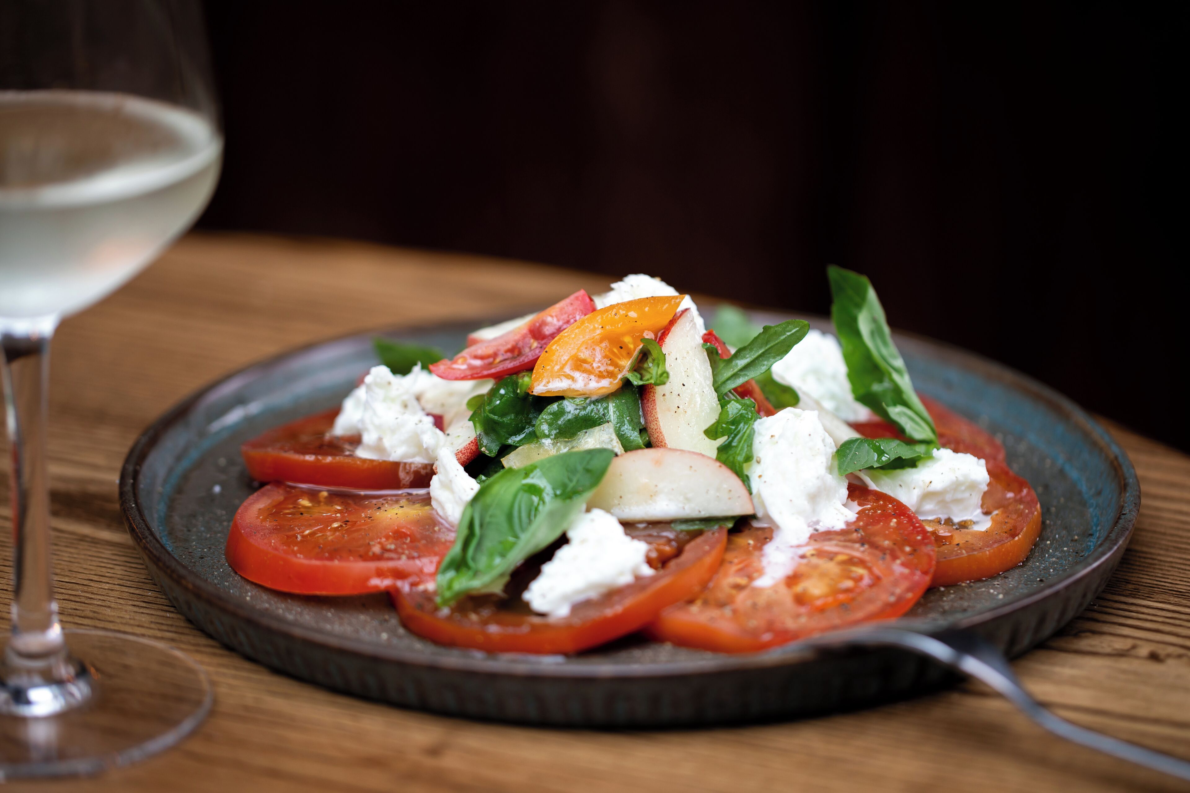 Ensalada fresca de tomate con queso y albahaca sobre una mesa de madera.