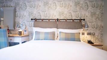 Una habitación de hotel con pared de piedra, una cama con almohadones a cuadros, una mesita de noche con lámpara y un espejo.