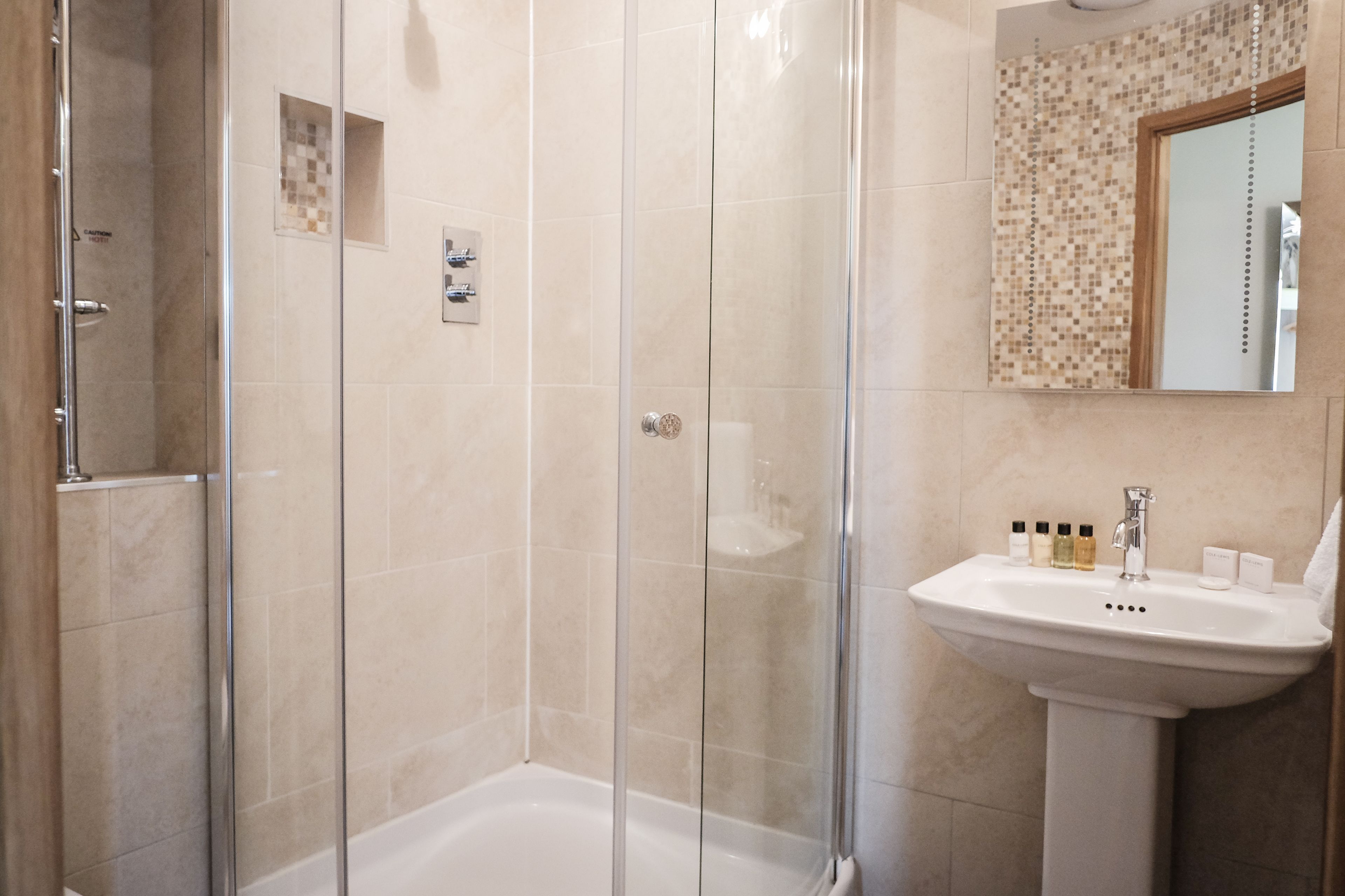 Un baño moderno con ducha acristalada, lavamanos pedestal y pared de azulejos con un espejo decorativo.