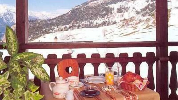 A table set with tea and snacks, a potted plant, and a view of snow-covered mountains. - Hôtel les Mottets (Aussois)