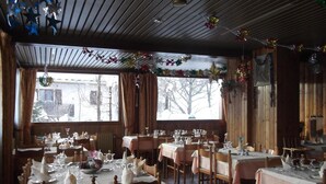 A restaurant with multiple tables set for dining, wooden walls, and large windows with a view of trees. - Hôtel les Mottets (Aussois)