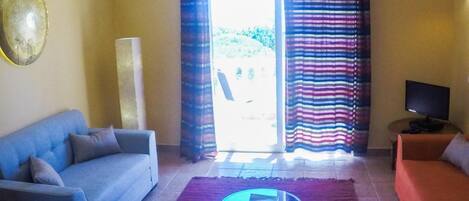 Una sala de estar con sofá, mesa de centro, televisor y ventana con cortinas.