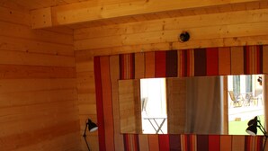 Ein Zimmer einer Holzhütte mit einem Bett, einem Spiegel und einem Fenster.