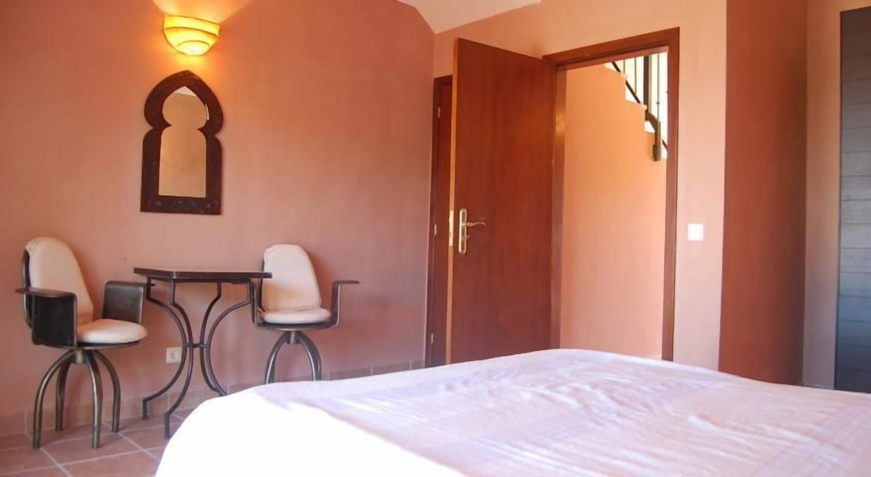 Een hotelkamer met een bed, twee stoelen, een tafeltje, een spiegel en een deur.
