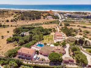 Vista aérea de um resort à beira-mar, com piscina, vários edifícios e uma praia ao fundo.