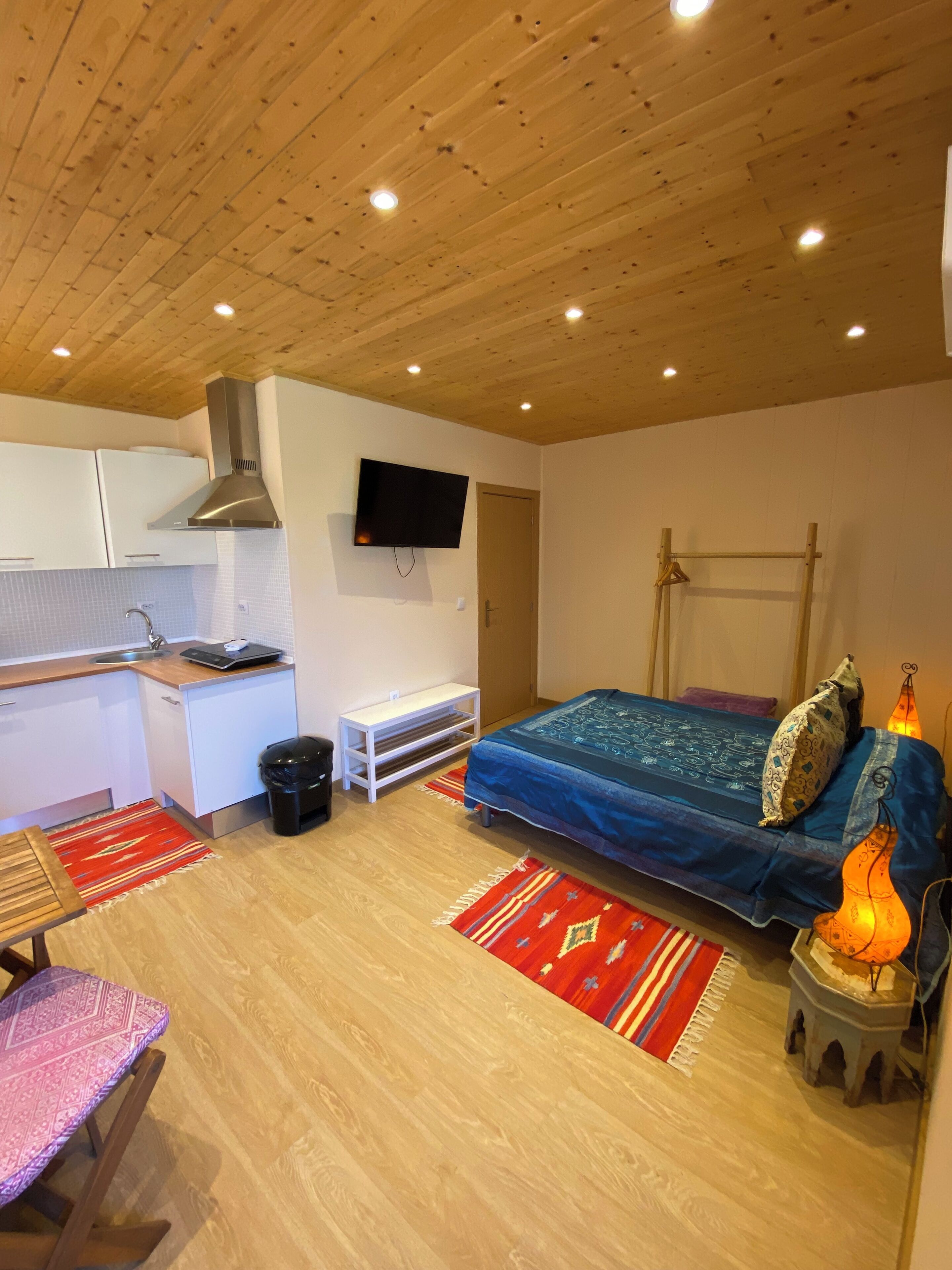 Ein gemütlicher Raum mit Küchenzeile, einem Bett, einem Fernseher und einem kleinen Tisch.