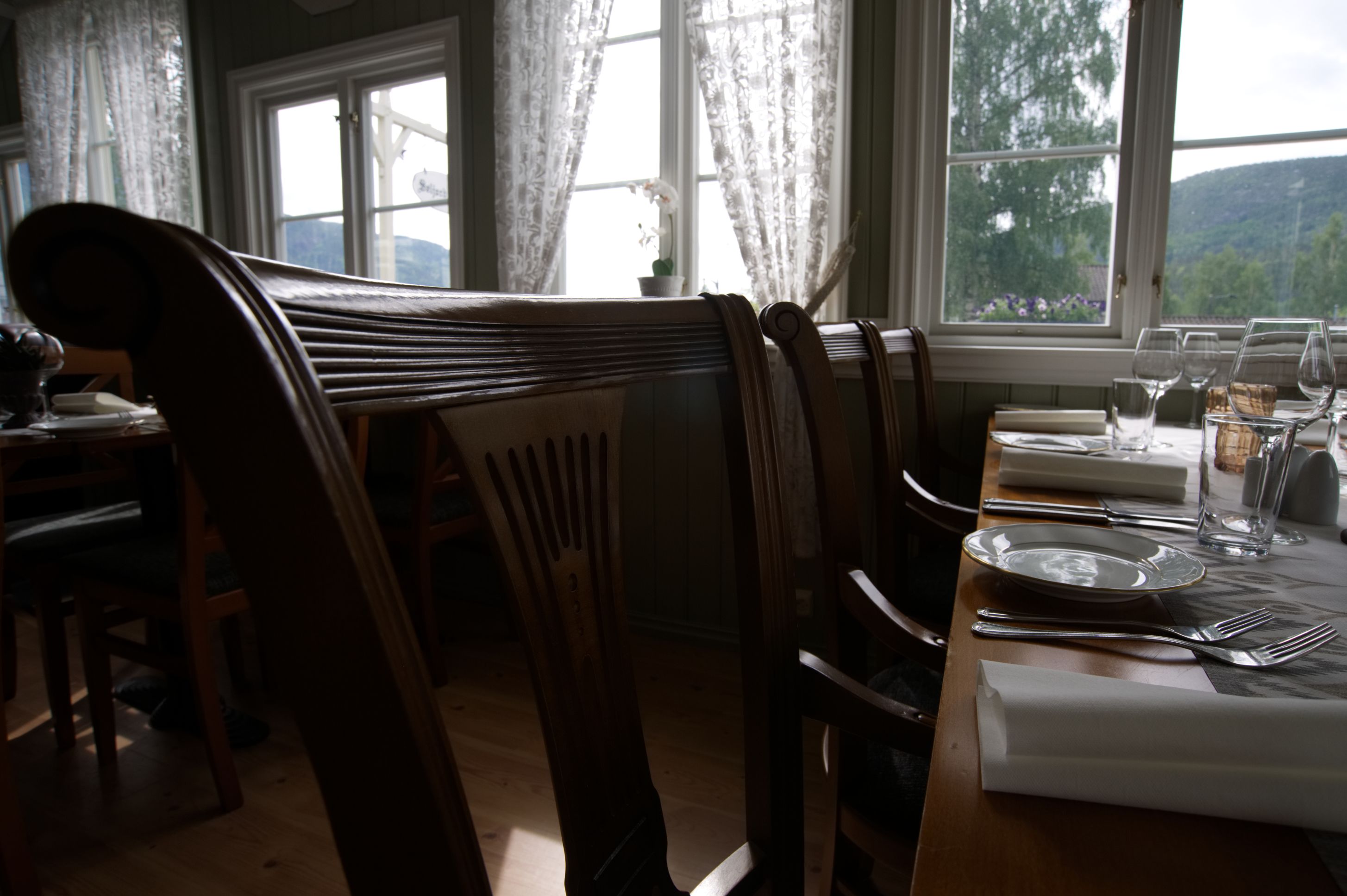 A dining area with wooden chairs and a table set for four, overlooking a scenic view.