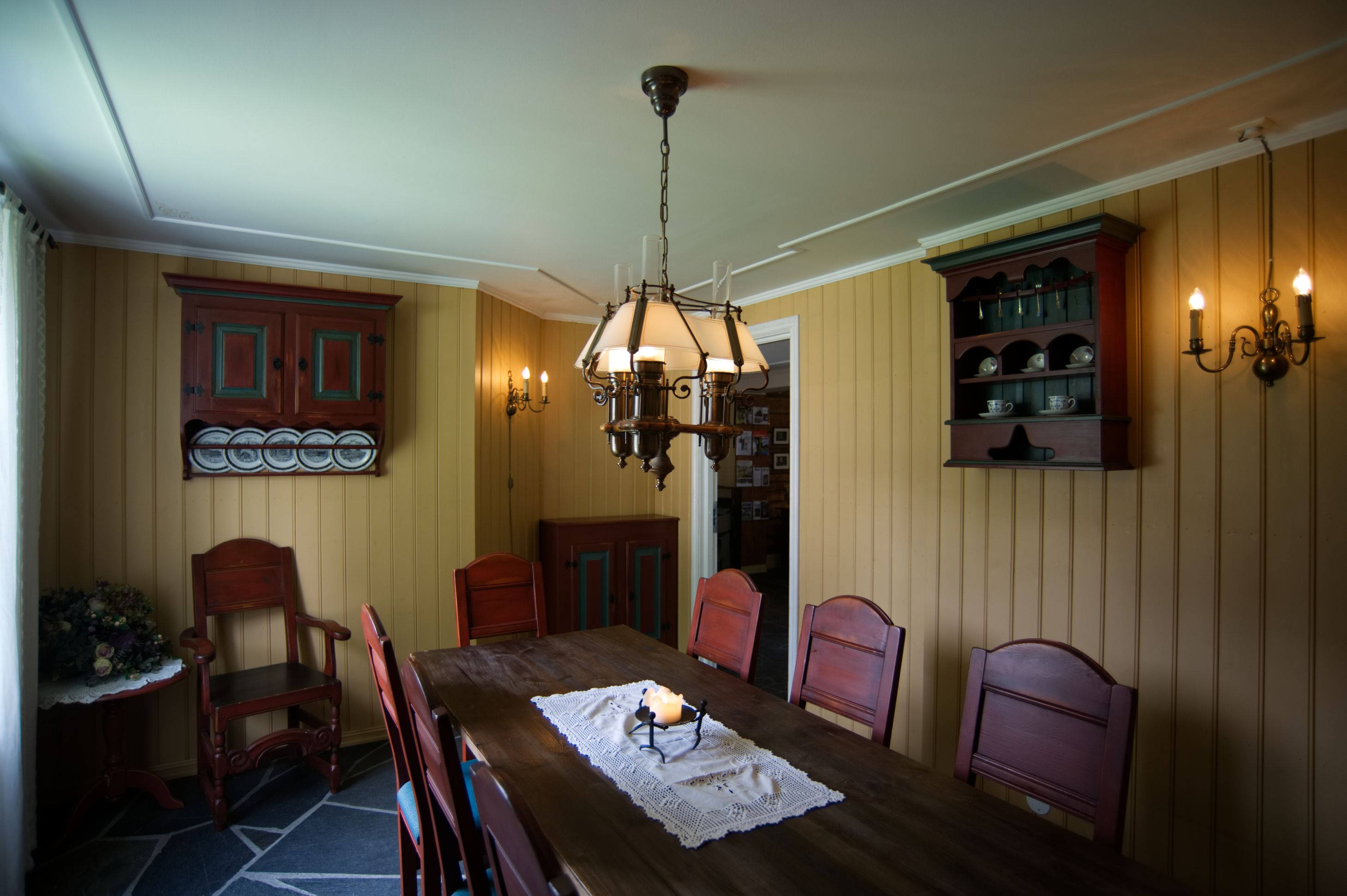 A dining room with a wooden table, chairs, a chandelier, and a china cabinet.