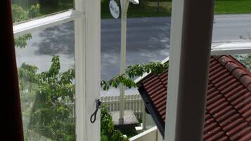 A view through a window with a white fence, a clock, and a red-tiled roof.