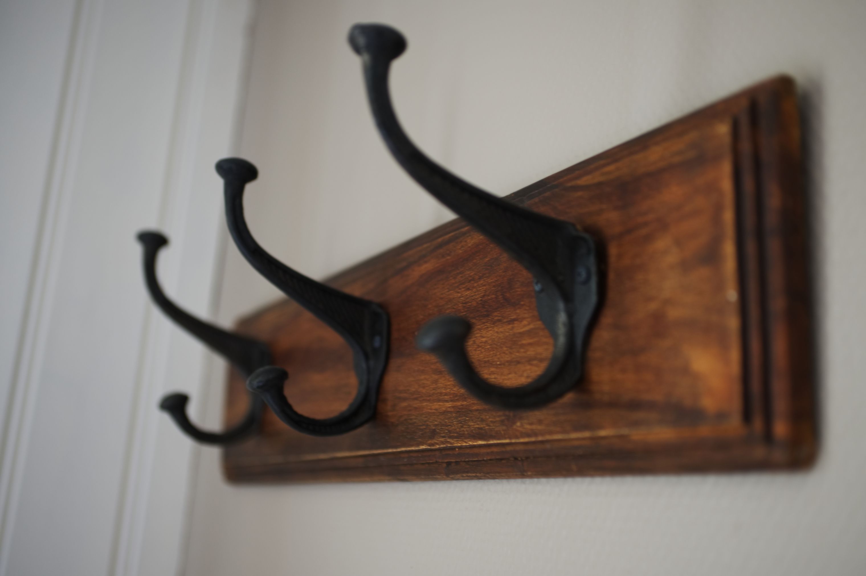 A wooden wall-mounted hookboard with three hooks.