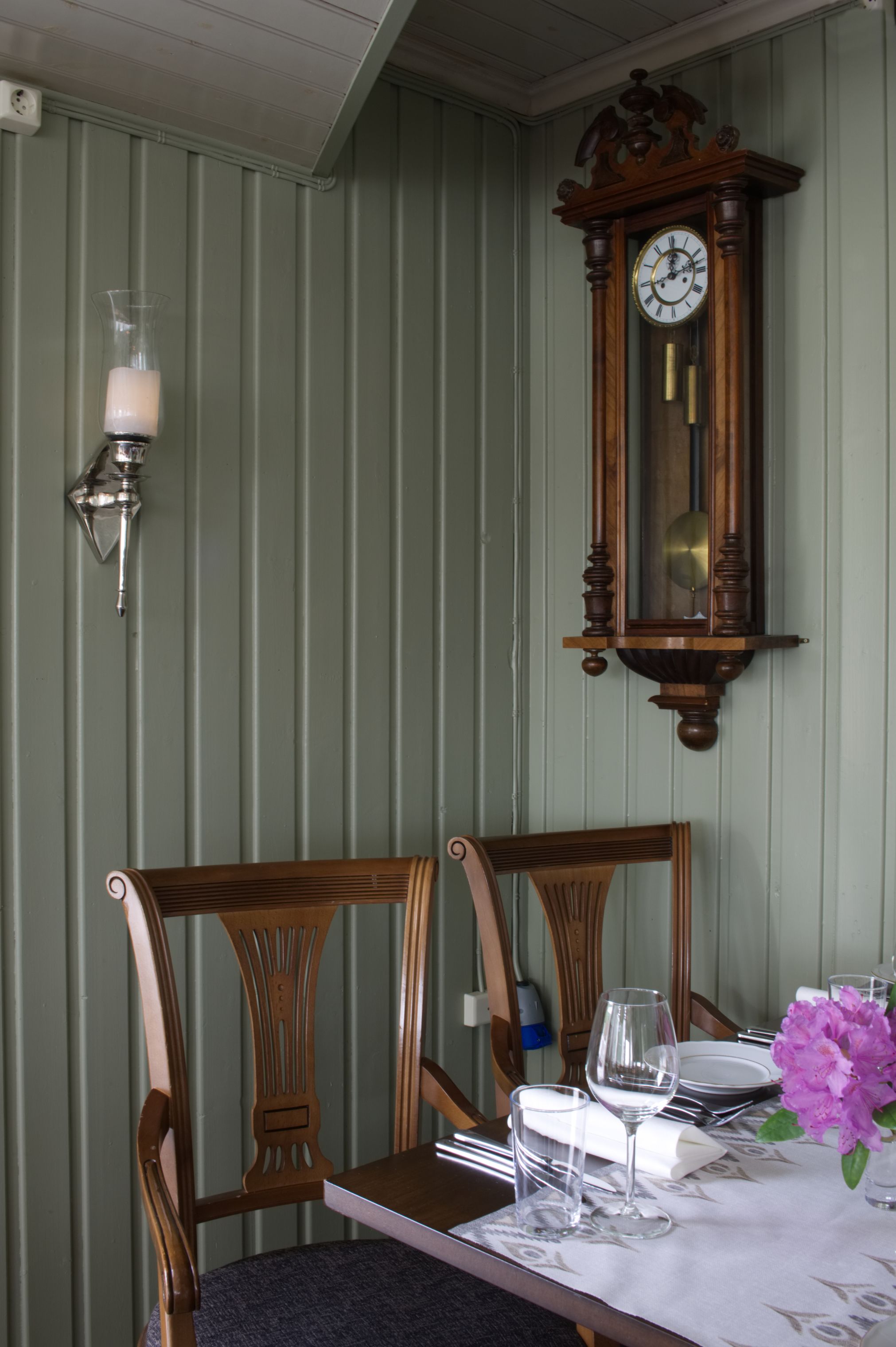 A dining table with chairs, a wall-mounted clock, and a wall-mounted light fixture.